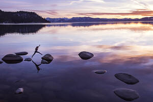 Frau springt bei Sonnenuntergang am Lake Tahoe von Fels zu Fels - CAVF94579