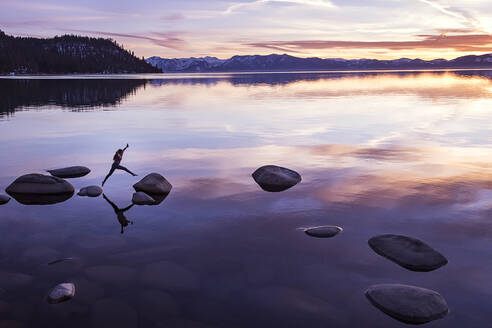 Female jumping from rock to rock at sunset on Lake Tahoe - CAVF94579