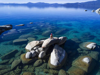 Young female sitting on rock in lake tahoe on sunny afternoon - CAVF94584