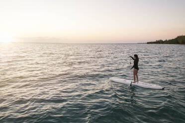 Junge asiatische Frau Paddleboarding in Bahamas bei Sonnenuntergang - CAVF94588