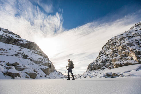 Rucksacktourist durchquert die Winterlandschaft zwischen zwei Bergen. - CAVF94610