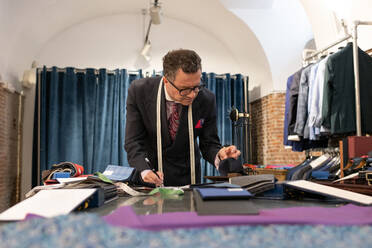 Mature tailor choosing fabric and making notes - CAVF94626