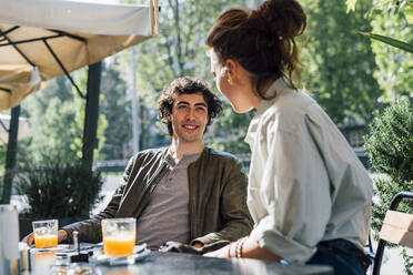 Smiling boyfriend sitting by girlfriend at sidewalk cafe - MEUF03187