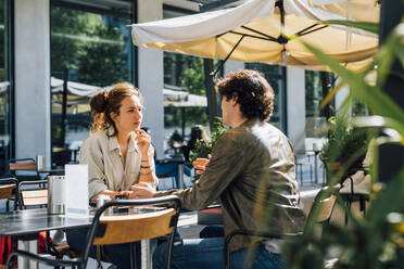 Couple talking while siting at sidewalk cafe on sunny day - MEUF03191