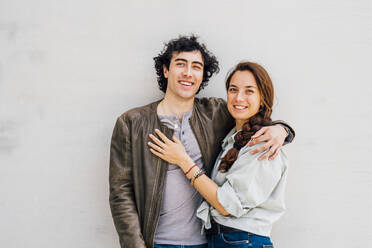 Smiling couple standing together in front of white wall - MEUF03203