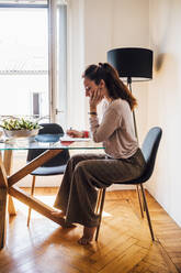 Woman writing on paper while working at home - MEUF03219