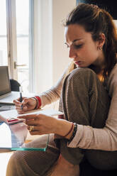 Woman writing in book while sitting by dining table at home - MEUF03221