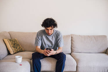 Man using mobile phone while sitting by coffee cup on sofa - MEUF03222