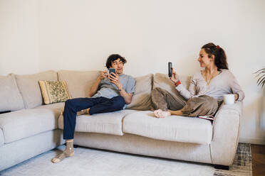Die Freundin fotografiert ihren Freund mit dem Smartphone, während sie zu Hause sitzt - MEUF03224