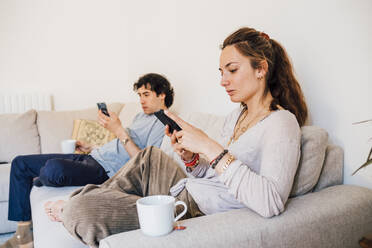 Ein Paar benutzt ein Mobiltelefon, während es zu Hause auf dem Sofa sitzt - MEUF03225