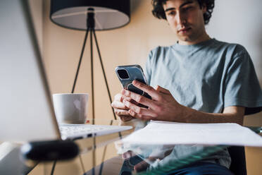 Man using mobile phone while sitting with laptop at table - MEUF03234