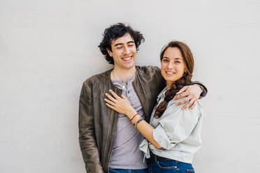 Smiling couple with arms around standing in front of wall - MEUF03247