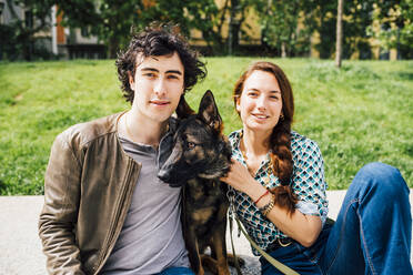 Smiling couple sitting by dog on footpath - MEUF03255
