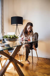 Woman checking book while sitting by dining table at home - MEUF03273