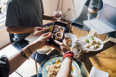 Woman photographing food through smart phone with man in background at dining table - MEUF03292