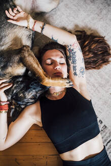 Woman resting with dog on carpet at home - MEUF03296