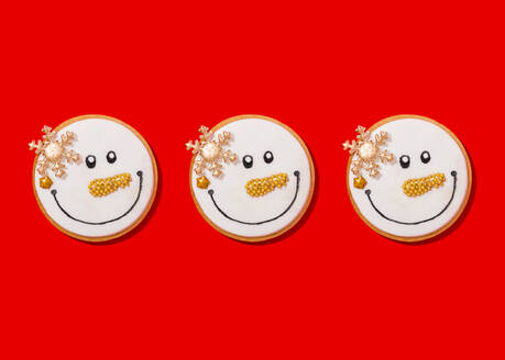 Three snowman shaped Christmas cookies against vibrant red background - FLMF00579