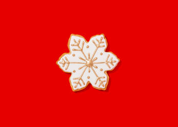 Snowflake shaped Christmas cookie against vibrant red background - FLMF00582