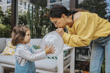 Mädchen sieht Mutter beim Aufblasen eines Luftballons im Hinterhof an - MFF08236