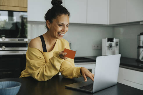 Smiling woman doing online shopping through credit card at kitchen island - MFF08241