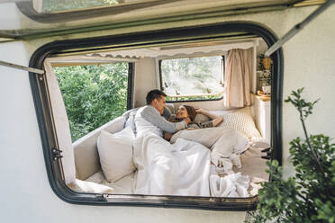 Loving man embracing girlfriend while lying on bed seen through camper window - VPIF04370