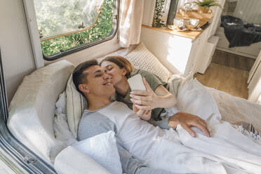 Frau küsst Freund und macht Selfie auf dem Bett im Wohnmobil - VPIF04376