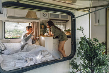 Young woman leaning on table looking at boyfriend drinking coffee in motor home - VPIF04378