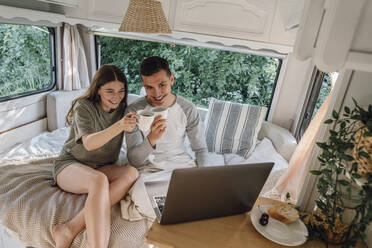 Glückliches junges Paar hält Kaffeetassen und führt einen Videoanruf über einen Laptop im Wohnmobil - VPIF04381