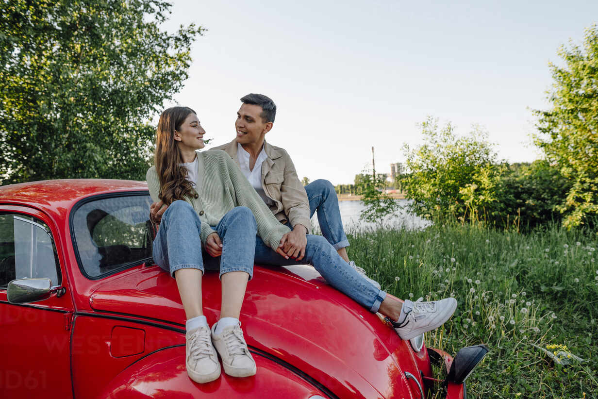 Young couple in love sitting on car bonnet stock photo
