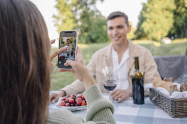 Young woman photographing boyfriend sitting at table - VPIF04413