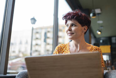 Nachdenkliche Frau, die mit ihrem Laptop in einem Café sitzt und wegschaut - JCCMF03110