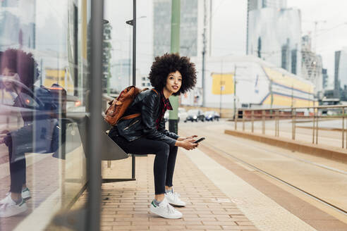 Frau mit Mobiltelefon an der Straßenbahnhaltestelle - MEUF03314