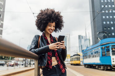 Happy woman using smart phone while leaning on railing - MEUF03320