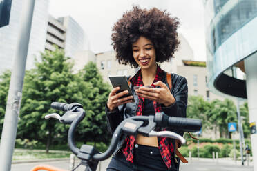 Smiling woman holding credit card while using mobile phone in city - MEUF03332