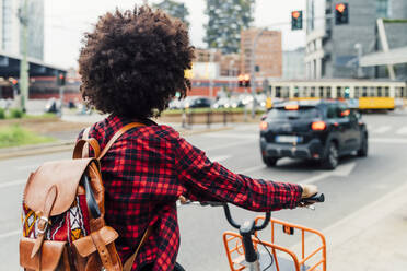 Junge Frau mit Rucksack auf dem Fahrrad in der Stadt - MEUF03335