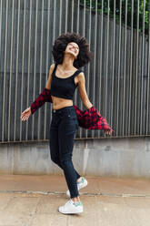 Glückliche junge Frau tanzt vor einer Wand - MEUF03350