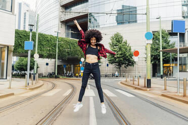 Cheerful woman with arms outstretched jumping on tracks in city - MEUF03351
