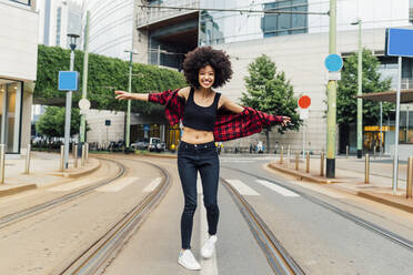 Happy woman with arms outstretched standing on tramway in city - MEUF03352