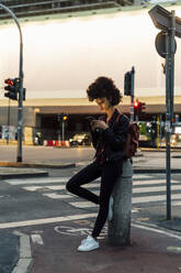 Young woman using mobile phone while leaning on bollard - MEUF03381