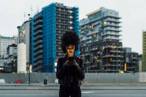 Frau, die ein Mobiltelefon benutzt, während sie in der Stadt steht - MEUF03384