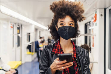 Frau mit Gesichtsmaske hält Mobiltelefon in U-Bahn-Zug - MEUF03391