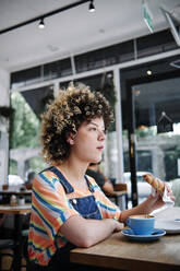 Frau isst Croissant, während sie am Tisch im Cafe sitzt - ASGF00740