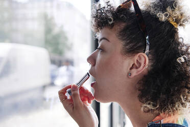 Junge Frau trägt in einem Café Lippenstift auf - ASGF00745