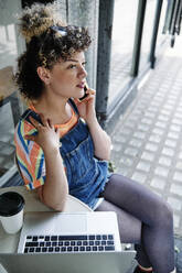 Young woman talking on smart phone while sitting at sidewalk cafe - ASGF00750