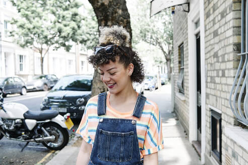 Smiling young woman looking down on footpath by building - ASGF00758