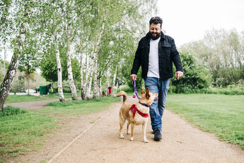 Lächelnder Mann mit Hund auf dem Fußweg im Park - ASGF00764