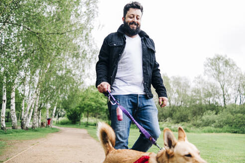 Mann hält Leine, während er mit seinem Hund auf dem Fußweg im Park spazieren geht - ASGF00765