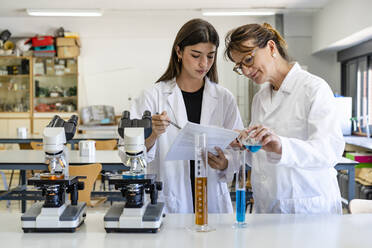 Eine Wissenschaftlerin liest ein Dokument, während ihr Kollege eine Flüssigkeit in einen Messzylinder gießt - DLTSF01977