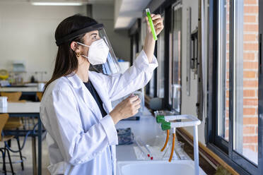 Junge Wissenschaftlerin mit Gesichtsschutzmaske bei der Untersuchung einer Chemikalie im Labor - DLTSF01985