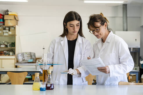 Eine Wissenschaftlerin liest ein Dokument, während sie einem Kollegen beim Experimentieren im Labor hilft - DLTSF01987